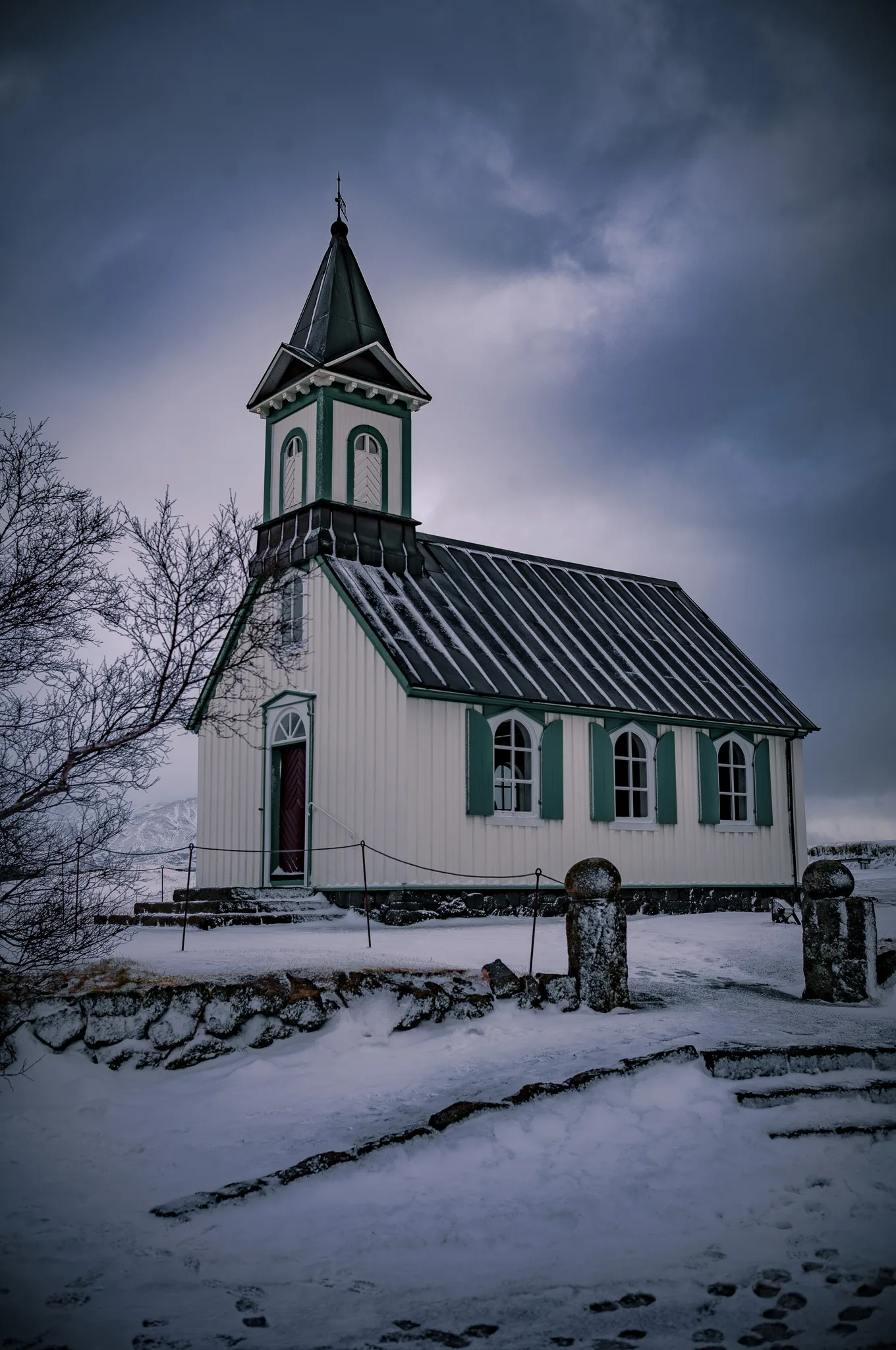 A lone white church stands against a dramatic Icelandic winter sky, snow blanketing the ancient valley of Þingvellir — one of the world's oldest parliaments.