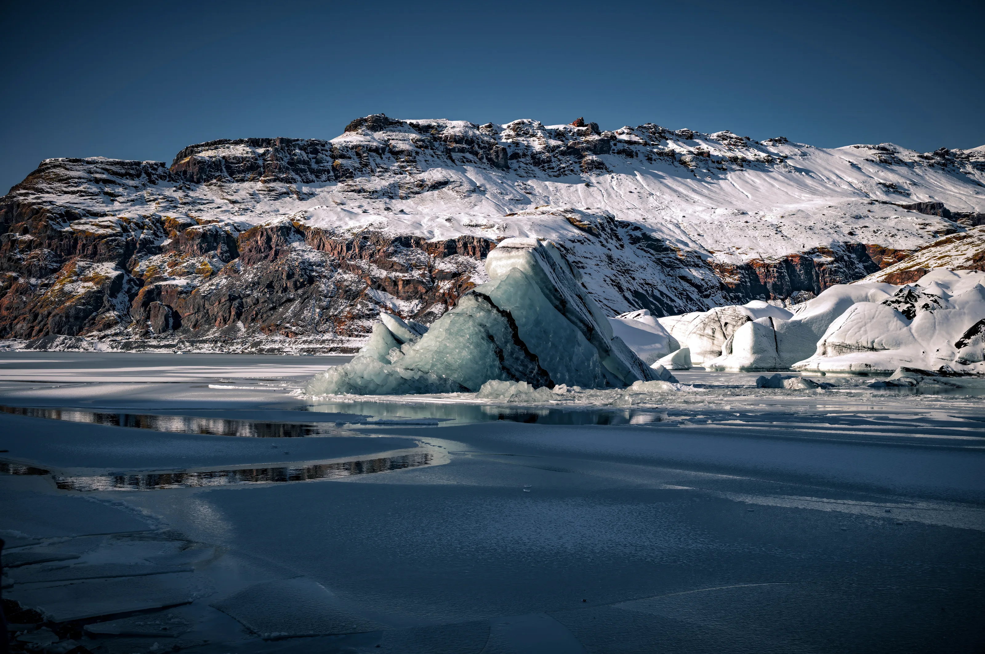 Floating blue ice drifts across a glacial lagoon, mountains mirrored in the still water. Iceland at its most elemental.